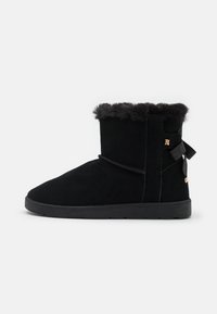 Stivaletto in suede nero con rifinitura in pelliccia sintetica, punta arrotondata e cinturino decorativo con logo sul lato. Suola in gomma piatta.