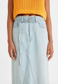 Falda de mezclilla azul claro con forma en A, que presenta un detalle de costura diagonal y un cordón en la cintura. Top corto de punto texturizado en naranja.