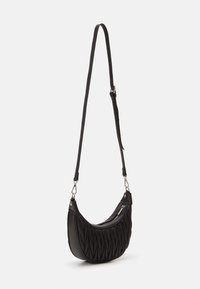 Sac à bandoulière noir en matériau texturé, avec une forme courbée, un design matelassé, des accessoires en argent et une sangle ajustable.