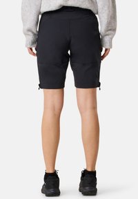 Svarta utomhusshorts med en avslappnad passform, elastisk midja och justerbara snören vid fållarna, kombinerade med svarta skor.