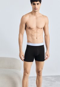 Čierne bavlnené boxerky s bielym elastickým pásom, na ktorom je logo "Calvin Klein". Dizajn je priliehavý a s dĺžkou po stred stehna.