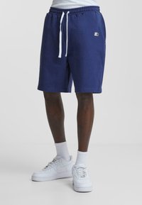 Navy sweat shorts with an elastic waistband and white drawstring, featuring side pockets and a small logo on the left thigh.