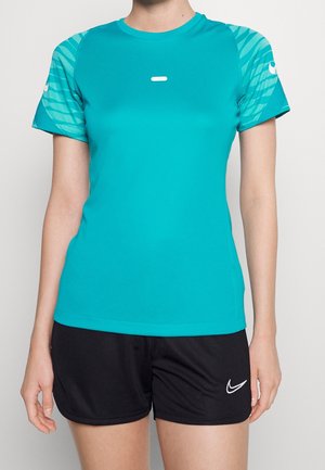 Osoba nosząca turkusową sportową koszulkę z krótkim rękawem i wzorzystymi rękawami oraz czarne sportowe spodenki z białymi logo Nike.