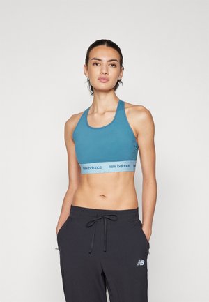 Sujetador deportivo en color azul verdoso con una banda elástica azul clara que presenta el logo de "new balance". El diseño incluye un corte de espalda nadadora y una textura simple y suave.