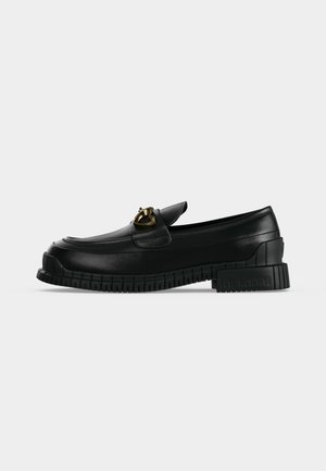 Mocassin noir chunky avec une épaisse semelle à rainures, une boucle en forme de cœur dorée sur le dessus, et "Love Moschino" embossé sur le talon.