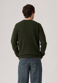 Groen sweatshirt van zachte stof, met een ronde hals, ribbelzoom en lange mouwen, gecombineerd met lichtblauwe, relaxte denim jeans.