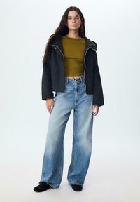 Čierna skrátená bunda s kapucňou a predným zipsom, skombinovaná s olivovo zeleným topom s dlhým rukávom a širokými svetlomodrými džínsami. Čierne topánky.