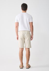 Light beige shorts with a drawstring waist, rolled cuffs, and two back pockets, paired with a plain white t-shirt and sandals.