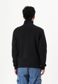 Sudadera negra con cuello alto, mangas largas y puños acanalados, combinada con pantalones cargo de color azul claro. Tejido suave, detalles mínimos.