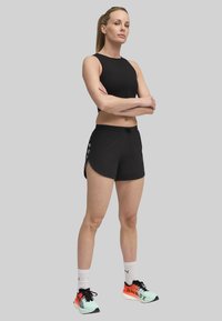 Sort ærmeløs top, sorte atletiske shorts med sideskæringer og mint- og orange sneakers med sorte accenter. Rent design, letvægtsmaterialer.