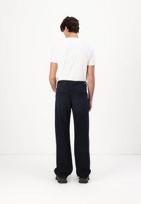 Mørkeblå denimjeans med rett ben, med baklommer og en subtil logo detalj på livet. Brukt med en hvit t-skjorte.