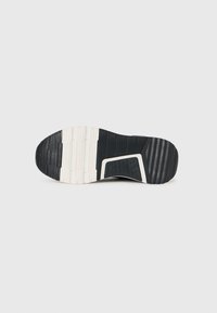 Semelle en caoutchouc noir de sneaker avec des motifs texturés, des rainures et une section distincte beige clair ; conçue pour la traction et la durabilité.