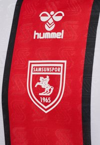 Czerwony sportowy trykot z białymi akcentami. Posiada centralne logo w kształcie tarczy z koniem oraz napisem "SAMSUNSPOR 1965" i białe logo "hummel" powyżej.