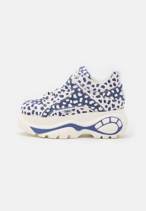 Masywne sneakersy z białym i granatowym wzorem w kropki, grubą białą podeszwą z granatowymi detalami i białymi sznurowadłami.