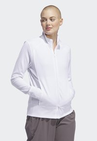 Jaqueta branca com fecho zip e fabricada em tecido texturizado, apresentando detalhes em canelado, bolsos laterais e um colarinho levantado. Ajuste standard.