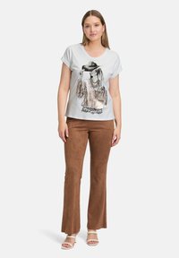 T-shirt gris clair avec une impression graphique d'une femme portant un chapeau. Associé à un pantalon évasé marron et des chaussures à lanières de couleur claire.