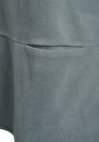 Svetlosivá fleecová látka s mäkkou textúrou, so zvislým švom a malým vreckovým detailom v spodnej časti.