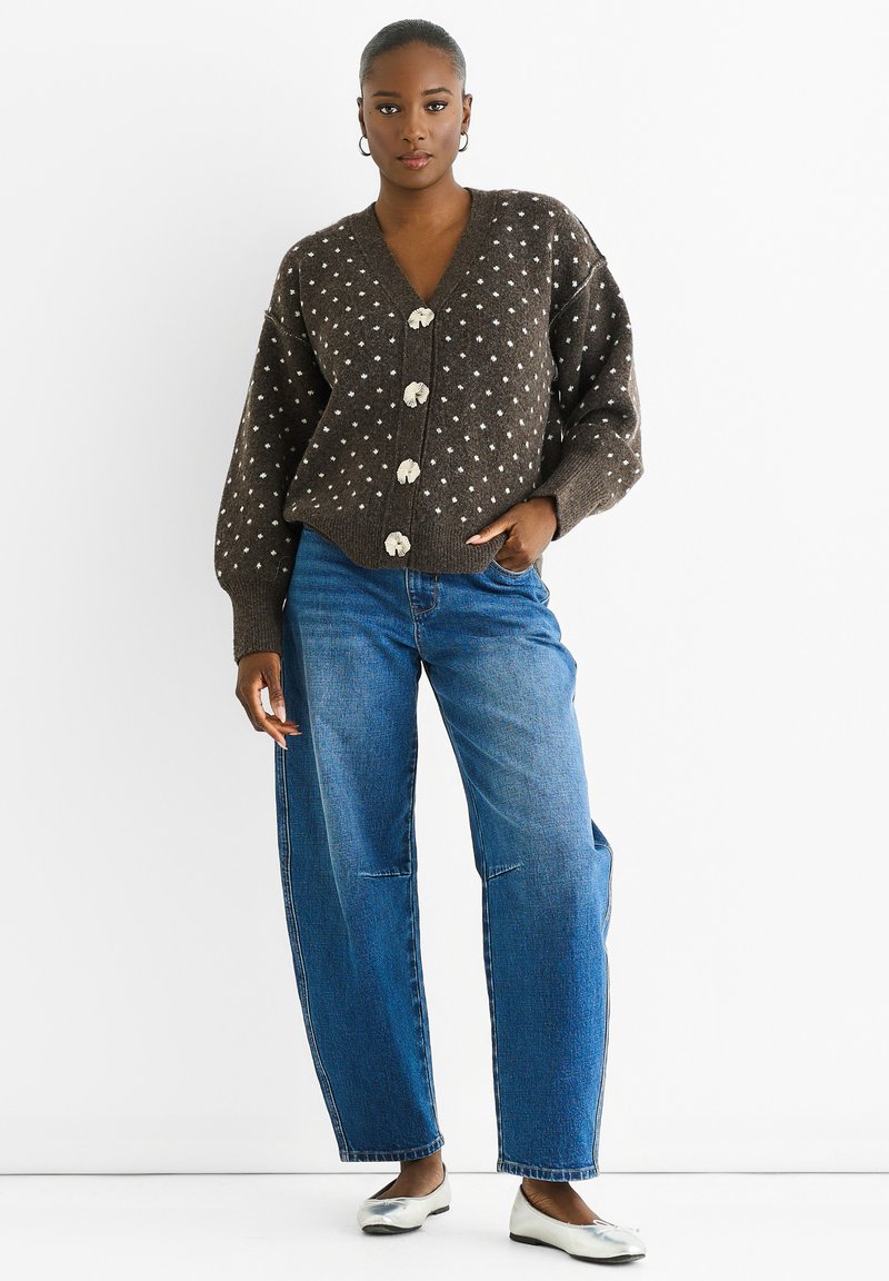Brown knitted cardigan with white polka dots, featuring a deep V-neck and large buttons, paired with blue wide-leg denim jeans and silver flats.