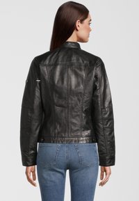 Zwarte leren jas met een aansluitend ontwerp, zichtbare naden en een hoge kraag. Gedragen over een paar blauwe jeans. Soepele textuur met minimale hardware.