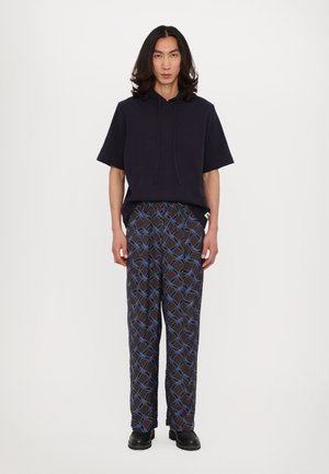 Felpa a coste blu navy con maniche corte e tasca frontale, abbinata a pantaloni neri a motivi con linee geometriche blu e bianche. Scarpe nere.