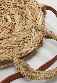 Borsa rotonda in paglia intrecciata con manici in ecopelle marrone. Colore naturale, superficie testurizzata e dettagli intrecciati intricati sui manici.