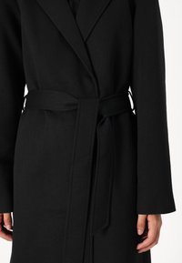 Svart ullblanding frakk med belted midje, notched lapels og lange ermer med en glatt tekstur. Minimalistisk design.