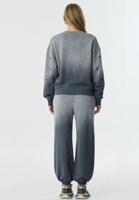 Grijze gradient sweater en bijpassende broek met elastische manchetten. De sweater heeft stipaccenten op de mouwen. Zacht, gestructureerd materiaal.