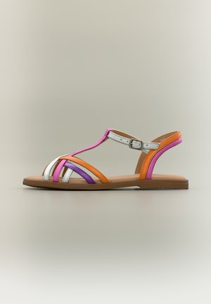 Sandale plate avec fines lanières en orange, rose, violet et blanc, équipée d'une boucle à la cheville et d'une semelle marron sur un fond neutre.