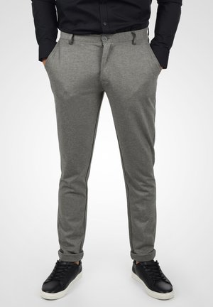 Pantalons gris en tissu texturé, à coupe slim, devant plat, poches latérales et rayures noires sur les côtés, associés à des baskets noires.