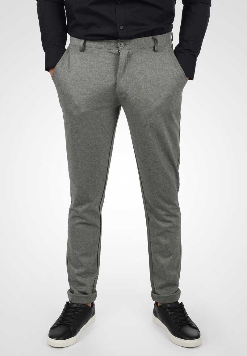 Szare spodnie z teksturowanej tkaniny, o slim fit, z płaskim przodem, bocznymi kieszeniami i czarnymi paskami po bokach, w połączeniu z czarnymi sneakersami.
