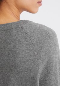 Γκρι πλεκτό πουλόβερ με στρογγυλή λαιμόκοψη, απαλό υφή και ραγκλάν μανίκια, με εμφανή ραφή στους ώμους.