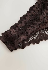 Nahaufnahme eines dunkelbraunen Spitzenstoffs mit Blumenmustern und gewellten Kanten auf hellem Hintergrund.