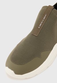 Scarpa slip-on verde oliva con tomaia in rete testurizzata, punta liscia e suola in gomma bianca a contrasto. Caratterizzata da una linguetta in tessuto.