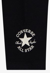 Tessuto nero con un logo circolare bianco che presenta una stella e il testo: "CONVERSE Chuck Taylor ALL STAR." Logo centrato nel design.