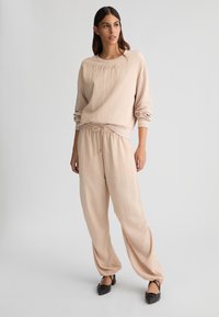 Felpa in cotone mélange beige chiaro con polsini a coste, caratterizzata da logo impresso. Abbinata a pantaloni larghi con vita regolabile dello stesso colore.