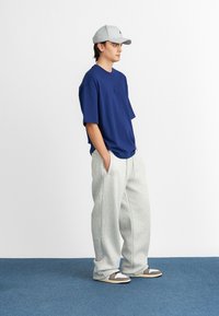 Námornícka oversized tričko s logom na hrudi, spárované s svetlo šedými teplákmi. Doplnky zahŕňajú svetlo šedú čiapku a voľnočasovú obuv.