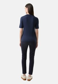 Námořnická krátkosrstá blůza s rovný střih, spárovaná s tmavými kalhotami a světle zabarvenými plyšovými bačkory, pohled zezadu.