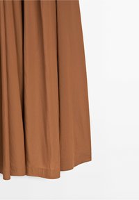 Jupe en tissu marron avec des plis doux et un ourlet soigneusement cousu sur un fond blanc uni.
