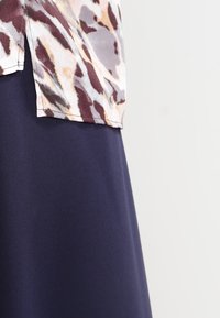 Top a maniche corte con un design di stampa animale astratta multicolore; sovrapposto a una gonna liscia, di un blu navy scuro, lunga fino al ginocchio.