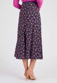 Jupe midi florale avec un fond bleu marine, ornée de fleurs roses et jaunes. Design évasé avec un ourlet fluide, associée à des talons rose clair.