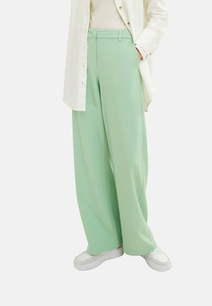 Wide-leg mint green trousers worn with a cream ribbed top, white long button-up shirt, and white sneakers.
