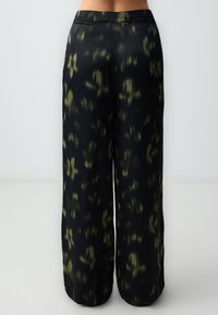 Zwarte wijde broek met een groen abstract patroon, een gladde textuur en een naadloze tailleband. Geschikt voor verschillende stijlen en gelegenheden.