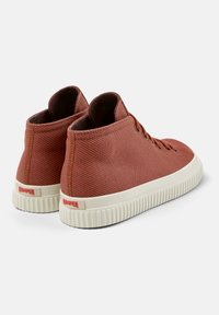 Red textured high-top sneakers with cream rubber soles and eyelet lacing, featuring a branded accent on the heel.