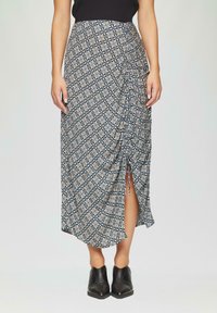 Jupe maxi bleu marine avec un imprimé floral, présentant un design froncé et une fente sur le côté. Assortie à des bottines noires.