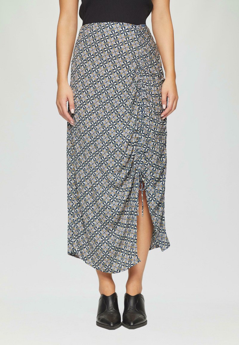 Jupe maxi bleu marine avec un imprimé floral, présentant un design froncé et une fente sur le côté. Assortie à des bottines noires.