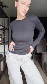 Maglia nera a maniche lunghe realizzata in tessuto liscio, abbinata a pantaloni della tuta grigi chiari, larghi, con tasche e cintura elastica.