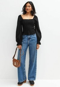 Top nero arricciato con maniche a sbuffo, abbinato a jeans a gamba larga blu a vita alta. Borsa a tracolla marrone e zoccoli neri con piattaforma.