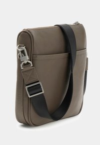 Compact taupe crossbody bag with black adjustable strap, front slip pocket, and silver metal clasp detail on light background.