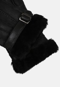 Black leather glove featuring a soft black fur cuff, with stitched detailing and a metal buckle accent. Smooth texture and fitted design.