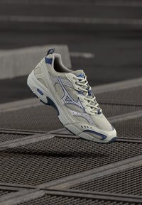 Light gray athletic shoe with mesh upper, blue accents, and a cushioned sole. Features a rounded toe and lace-up closure with logo detail.